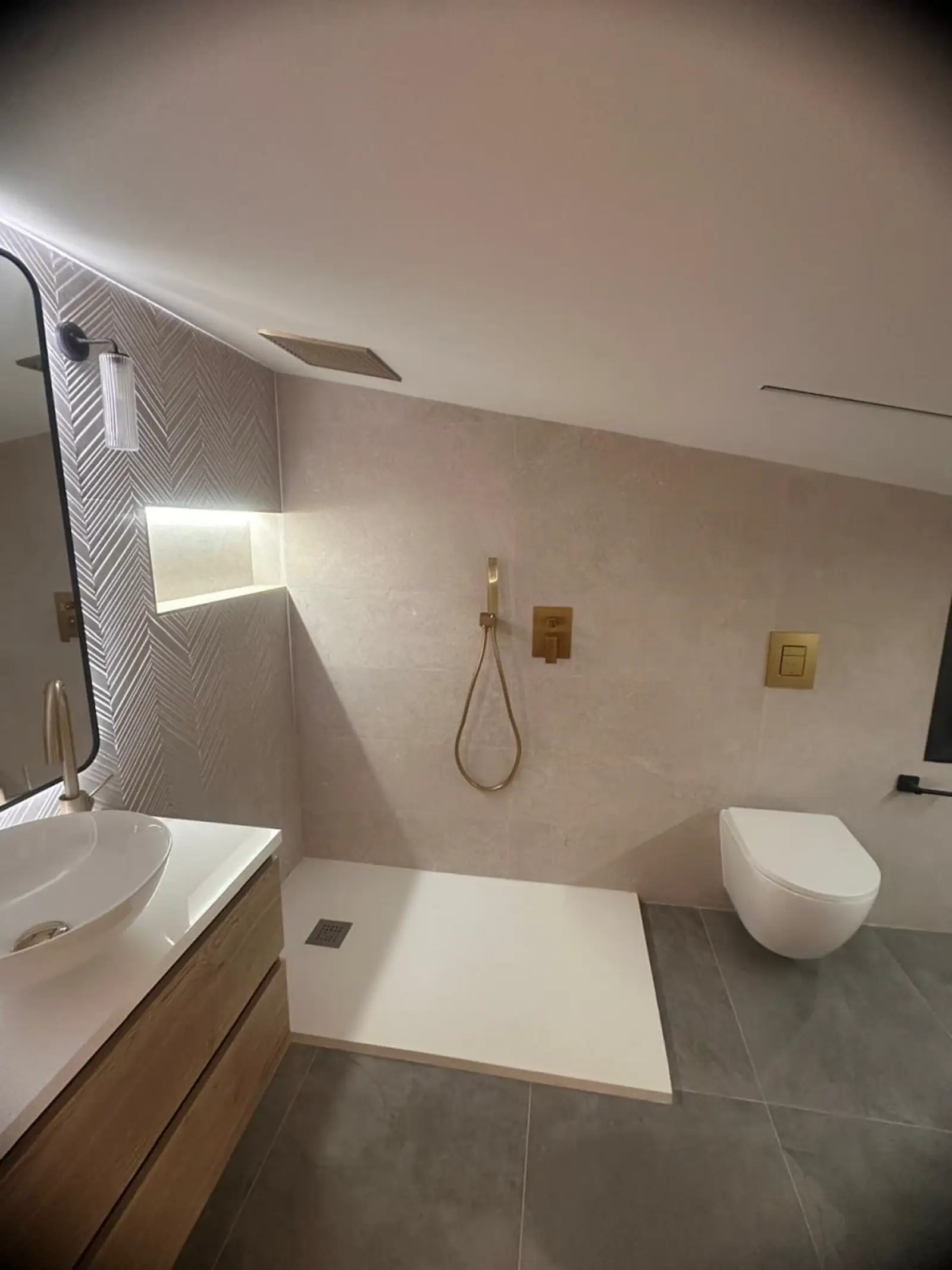Baño reformado bajo cubierta con plato de ducha, sanitario suspendido y grifería empotrada