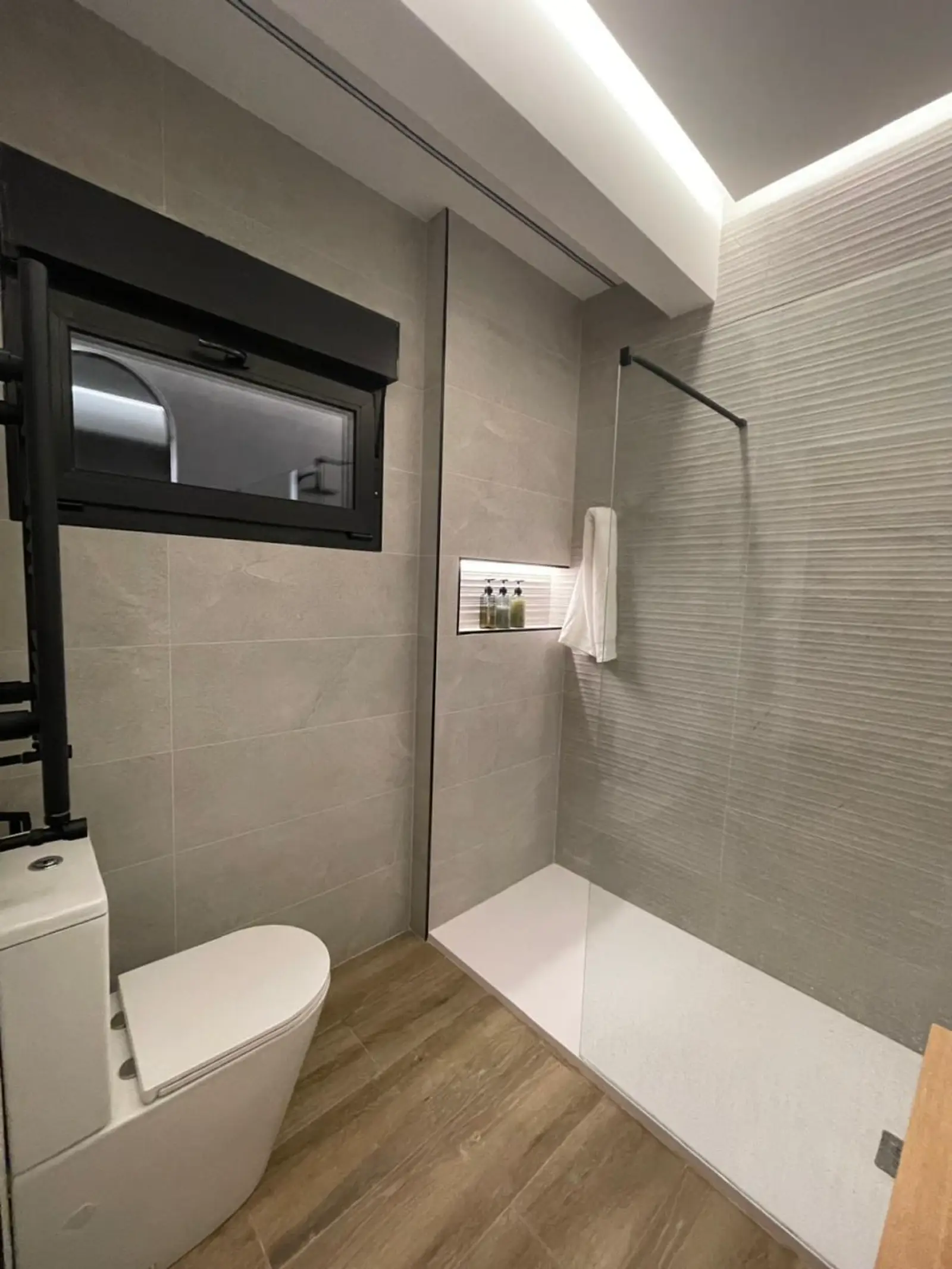 Baño reformado con ducha abierta, ventana negra, hornacina iluminada y revestimiento gris