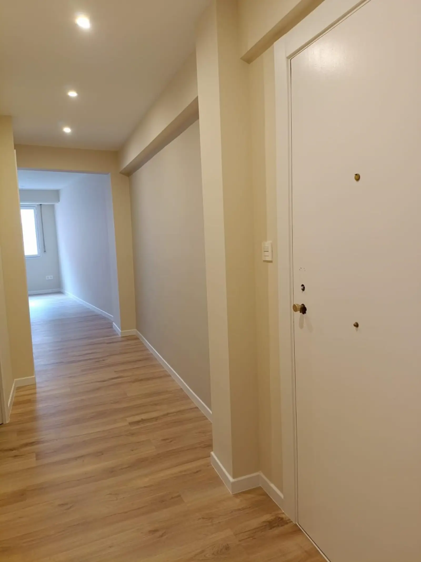 Pasillo reformado con suelo laminado, puertas blancas e iluminación empotrada